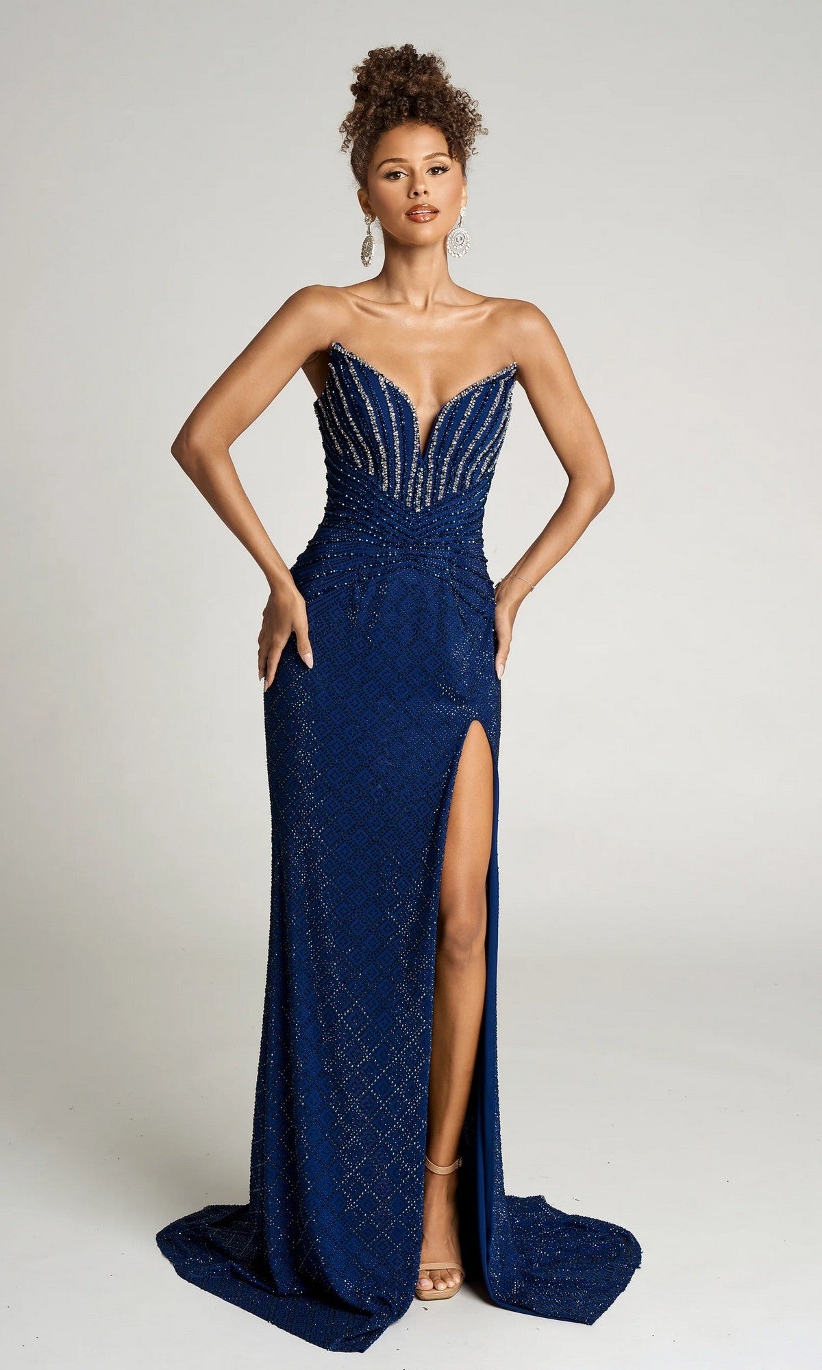 A woman stands in a neutral studio wearing the Portia and Scarlett PS26016 long formal dress in navy, featuring a fitted strapless silhouette with beading, sweetheart neckline, and high slit—a stunning red carpet choice.